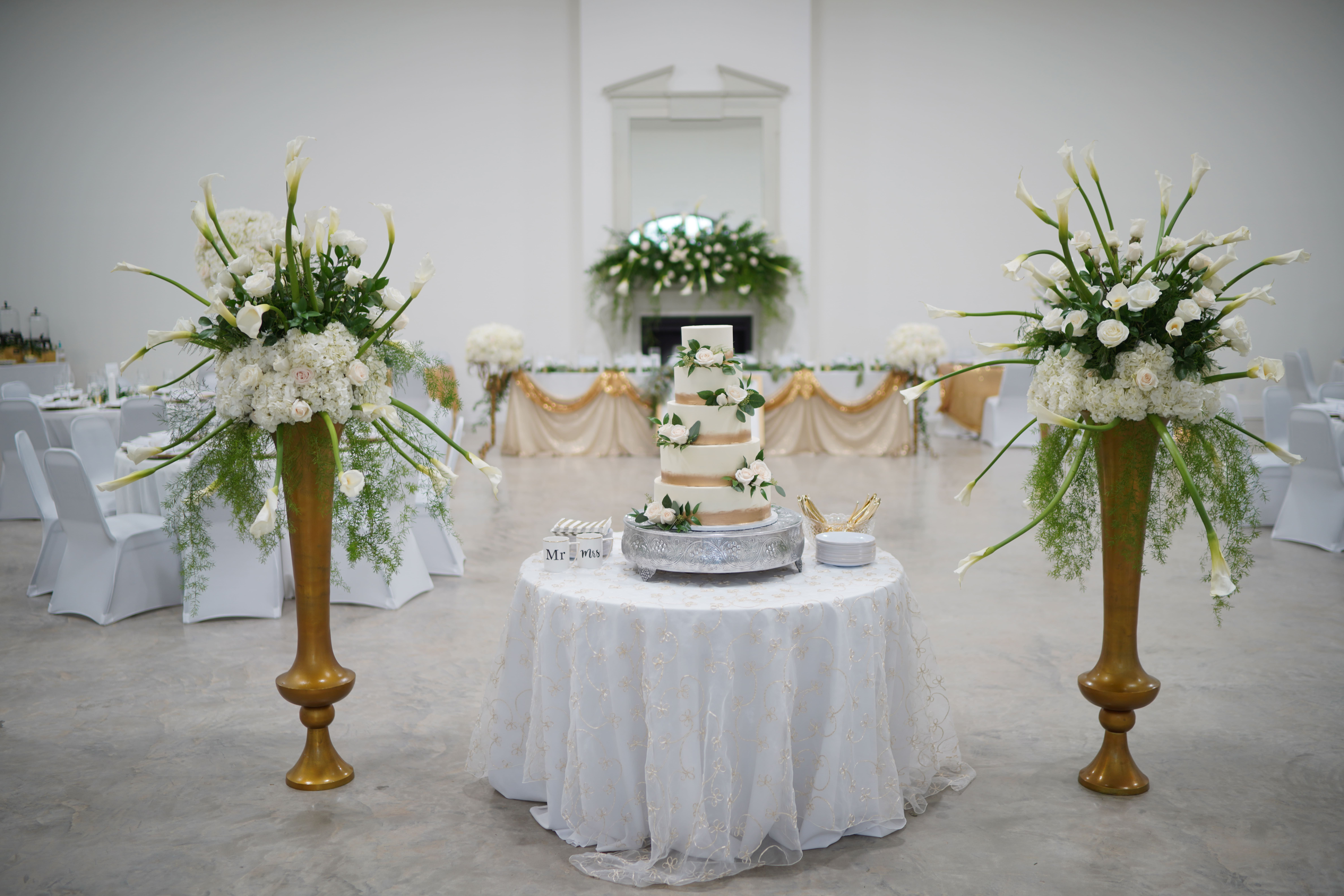 wedding cake with white flowers surrounded by large floral arrangements
